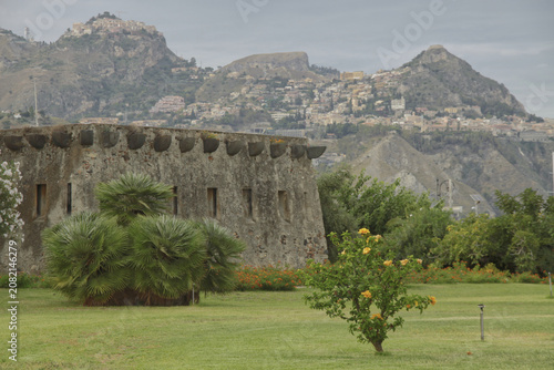 Historische Festungsmauer im Archäologischen Park Giardini Naxos mit Blick auf die Bergstadt Taormina in Sizilien