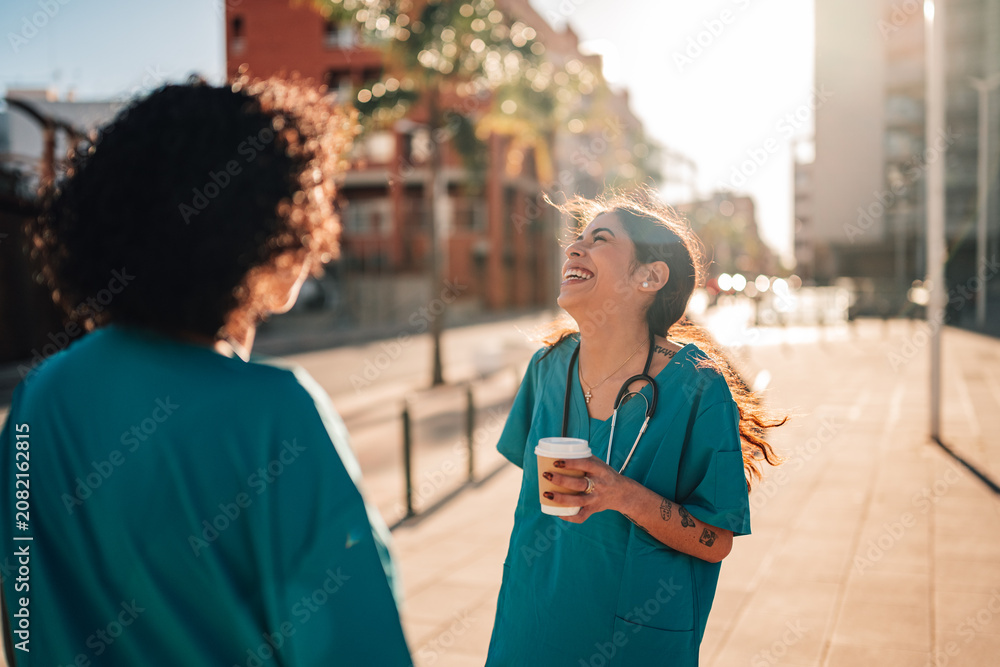 Fototapeta premium Happy medical professionals smiling and laughing during a coffee break, enjoying conversation on a city street at sunset