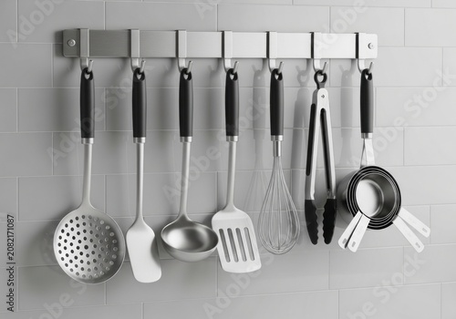 Monochrome image of stainless steel kitchen utensils hanging neatly on a wall mounted metal rack.