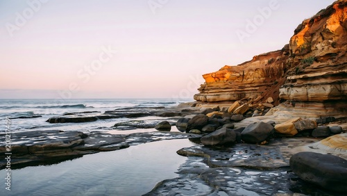 Rugged coastal cliffs meet the gentle ocean waves at sunset under a pastel sky