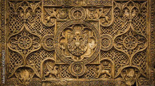 Quadro su tela Ancient gothic stone carving with heraldic symbols and intricate patterns in warm tones