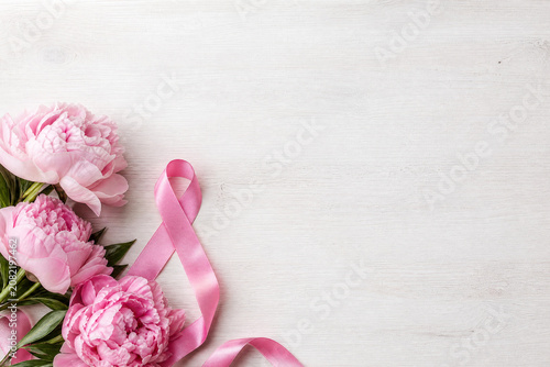 Flores de peônia cor-de-rosa e laço de conscientização sobre madeira clara com amplo espaço para texto - Conceito de beleza, sensibilidade e luta contra o câncer de mama.