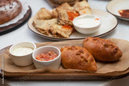 Freshly fried stuffed pies served on wooden board with sour cream and sauce, styled as traditional homemade comfort food.