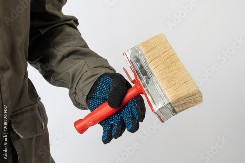 Close-up of a worker wearing gloves and holding a wide paint brush, illustrating home renovation, decorating and construction work.