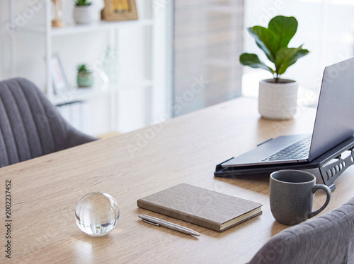 Schilderij op canvas Clean and minimalist home office desk featuring a clear glass sphere, a notebook, a pen, a coffee mug, and a laptop