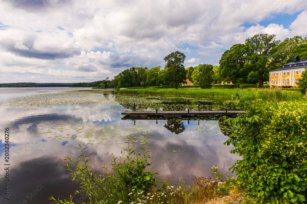 Fototapeta premium Beautiful view of lakeside pier with reflections and historic manor beside tranquil water. Sweden.