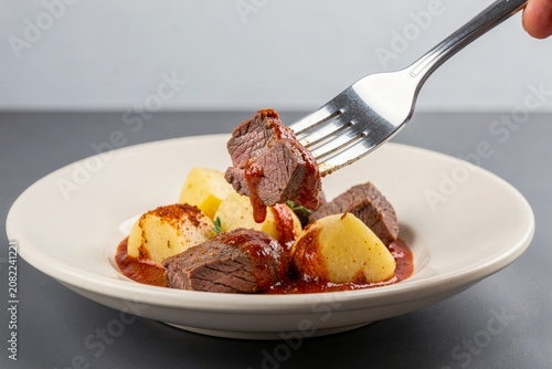 Gulas Czech served on white plate with beef stew, diced potatoes, and rich sauce. Concept of savory meal showcasing beef stew with paprika onions dumplings.