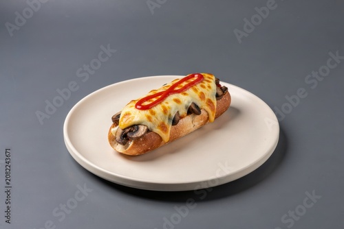 Zapiekanka topped with melted cheese, sliced mushrooms, and drizzle of ketchup on toasted baguette. Concept of comfort food featuring toasted baguette with mushrooms cheese ketchup.