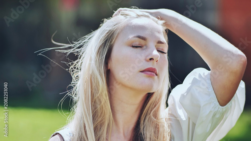 Foto Blonde woman basking in sunlight, eyes closed, hand gently touching hair, experi