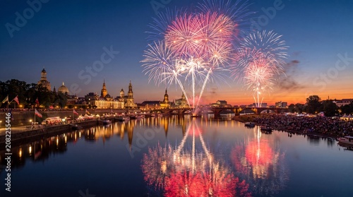 Fireworks display over river with historic buildings and crowd on the bank