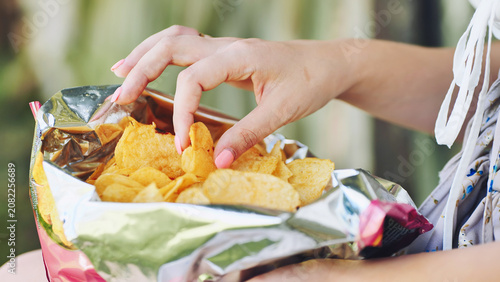 Fotografie Woman munching crispy potato chips, hand diving into bag, relishing salty crunch