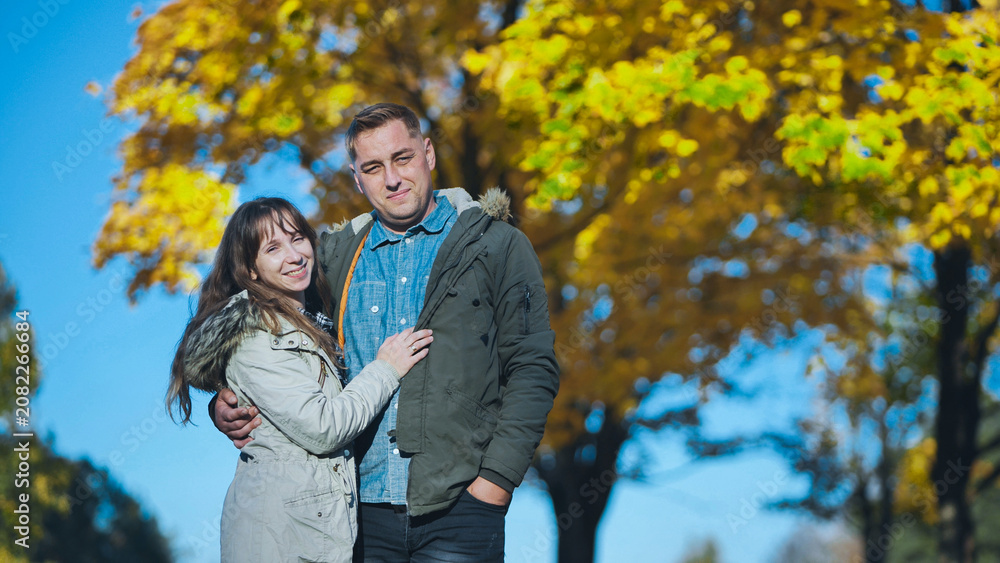 Fototapeta premium Romantic couple enjoying a sunny autumn day in a park with colorful foliage, embracing and smiling