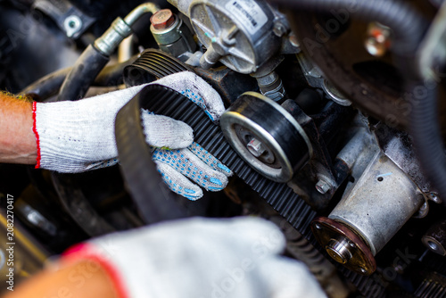 A mechanic wearing white gloves inspecting a black toothed timing belt inside a car engine. auto repair diagnostics, vehicle maintenance service, professional garage work.