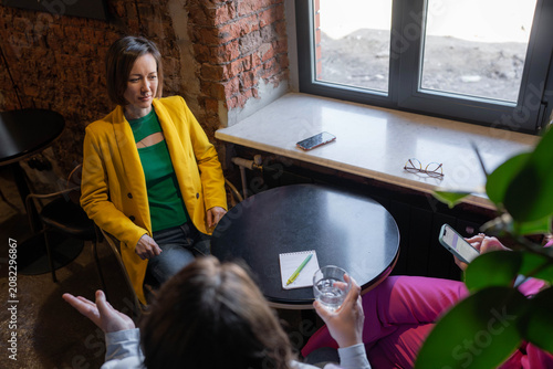Photos Top-down view of businesslike women in yellow and white meeting by window in cozy cafe nook