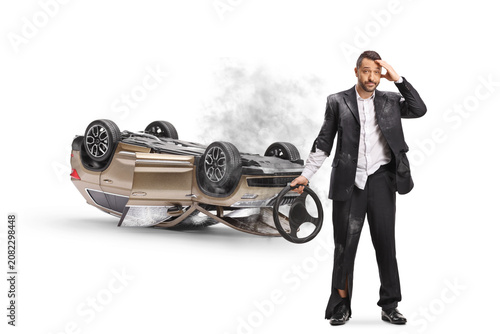 Fotografie Shocked driver holding a steering wheel next to an overturned car