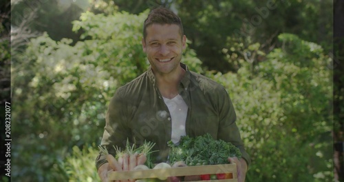 Gardener smiling down at produce holding crate in sunlit yard adjusting grip and presenting harvest