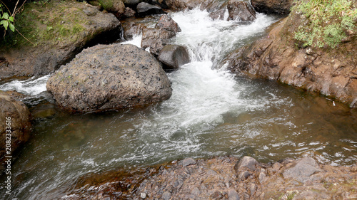 Bild auf Leinwand Freshwater stream flowing between textured rocky banks and stones, showcasing the natural beauty of an untouched mountain river