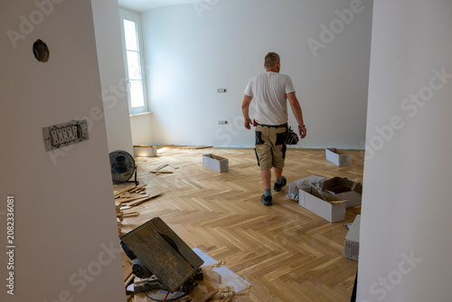 Stacks of engineered oak parquet planks prepared for installation inside bright renovated room with completed herringbone hardwood flooring and construction materials