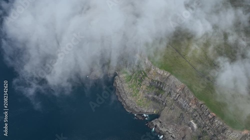 Drone shot of clouds falling down a steep coastal cliff on Suðuroy, Faroe Islands