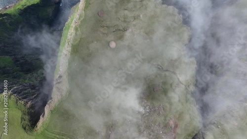 Drone shot of clouds falling down a steep coastal cliff on Suðuroy, Faroe Islands