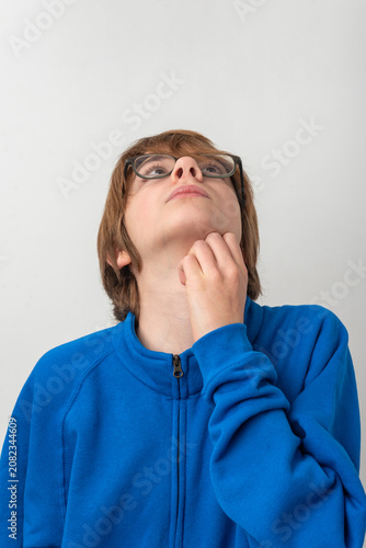 Young person with glasses wearing a blue sweatshirt, looking up with a thoughtful expression, scratching chin while contemplating new ideas or solutions