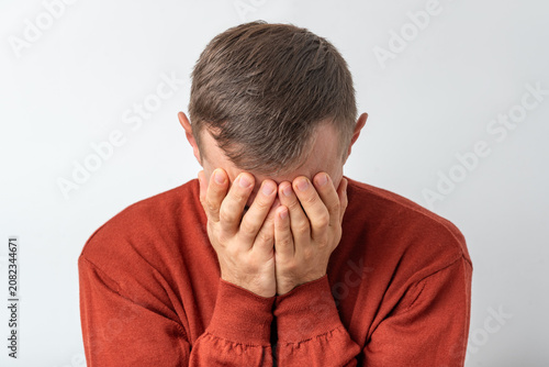 Man covering face with hands, expressing intense emotions of sadness, stress, and disappointment on a plain background, creating a powerful depiction of mental health struggles