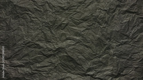 crumpled black paper texture shifts subtly under soft studio lighting creating a dramatic abstract background
