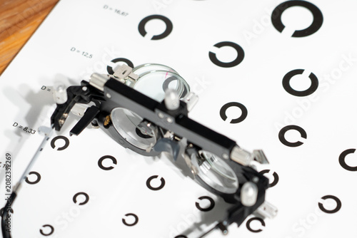 Close-up of a Snellen eye chart with black circular symbols. Medical vision testing device with adjustable lenses rests on the chart. Equipment measures visual acuity during eye exams