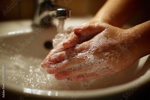 Foam and water droplets on a child's hands while scrubbing at a sink to promote hand hygiene awareness