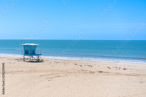View of a blue lifeguard tower standing on the sandy beach facing the blue ocean horizon under a clear sky in California