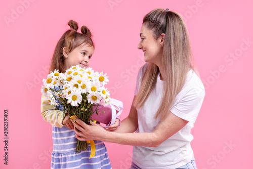 Little girl presenting bouquet of beautiful chamomile flowers and gift box to...