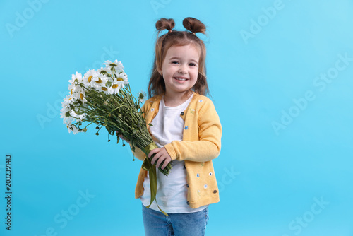 Cute little girl with bouquet of beautiful chamomile flowers on light blue ba...