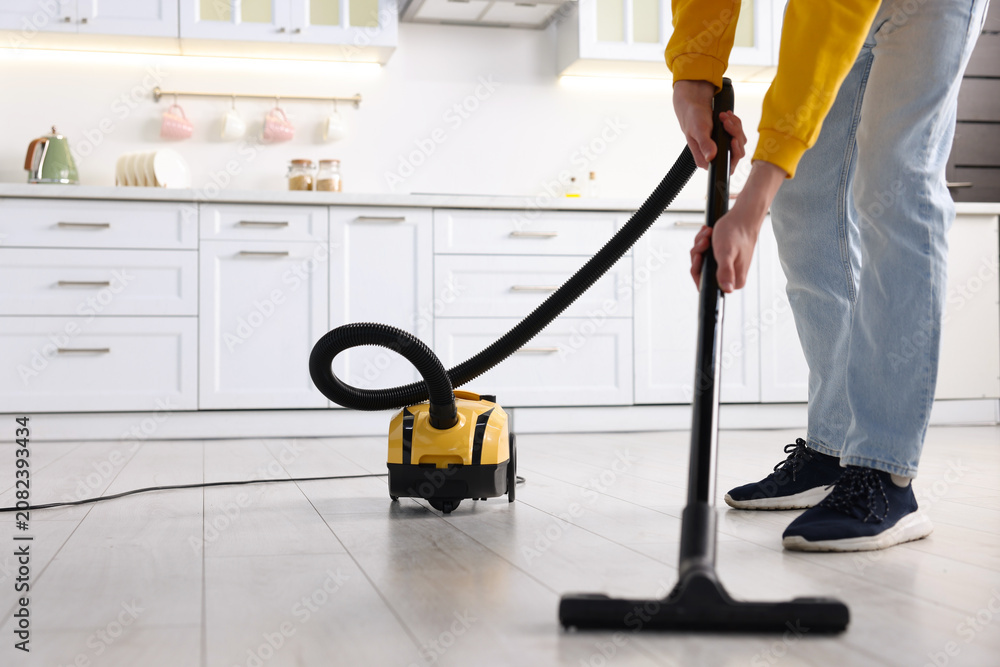 Fototapeta premium Housework. Teenage boy cleaning floor with vacuum cleaner in kitchen, closeup