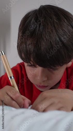 Young boy writing in notebook while resting on bed, highlighting relaxed learning, creativity and childhood education
