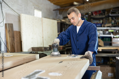 Billede på lærred Man sanding a wooden board using a sanding machine