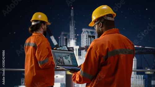 фотографія Offshore platform workers using map on laptop to circumvent embargo slowing fuel extraction operations, drilling rig colleagues searching for alternate maritime routes during oil crisis, camera A