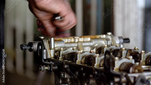 Close up view of mechanic hands using a socket wrench tool to repair or assemble a car cylinder head. Oily metallic automotive engine parts inside a mechanical workshop or garage. Professional vehicle