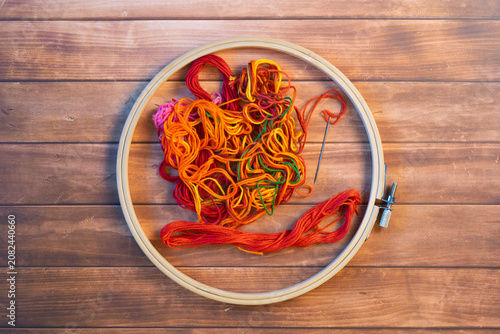 Принти на полотні An embroidery hoop encircles a needle and floss in shades of red, orange, and yellow on a brown background
