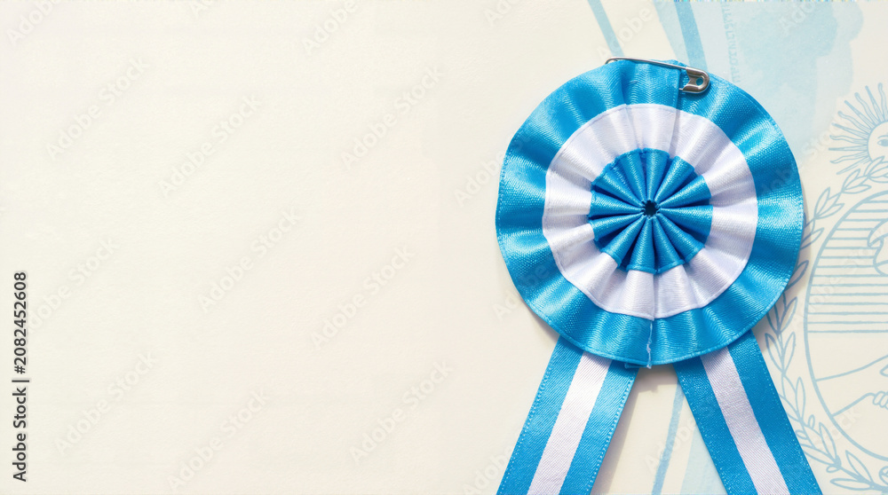 Obraz premium Argentine cockade ribbon on light background. Blue and white escarapela with copy space. Argentina independence day concept