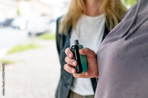 Schilderij op canvas In his hands is a compact gadget - an electronic cigarette or vape in turquoise (mint) color with a black mouthpiece or top panel