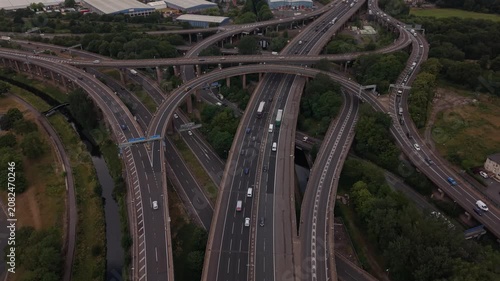 Drone flying backward over the iconic Spaghetti Junction motorway interchange in Birmingham, England. The aerial footage reveals multiple elevated M6 carriageways, sweeping curved flyovers, moving tra