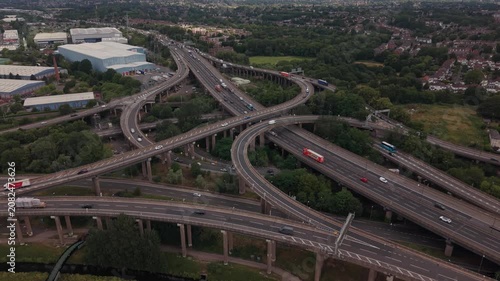 Low-altitude drone footage flying over the famous Spaghetti Junction interchange in Birmingham, England. The camera captures multiple elevated M6 motorway bridges, curved flyovers, moving traffic 
