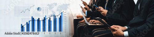 Принти на полотні Group of professionals immersed in data and technology with smartphones and laptops in a corporate environment, showcasing graphs and charts, symbolizing progress