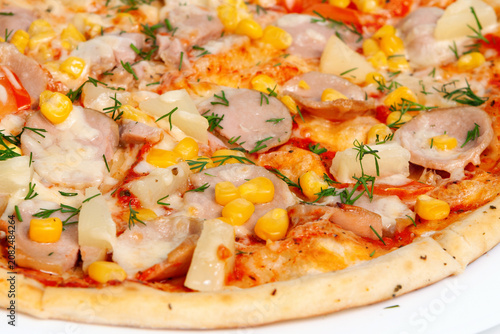 A closeups shot of baked pizza toppings with sliced sausages corn pineapple pieces and fresh herbs.savory dinner dish meal. Dining