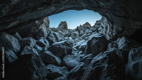 A dimly lit cave passage with rough stone walls and a small opening at the top for light
