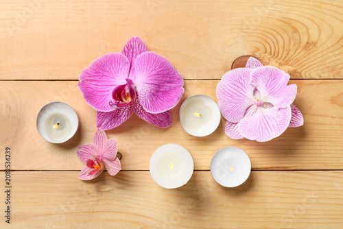 Fotografie Pink orchid flowers with lit tealight candles on wooden surface
