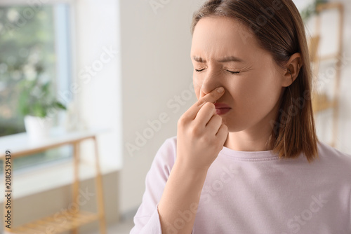 Photos Young woman holding nose with unpleasant expression indoors