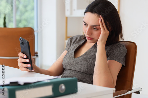 Foto Worried woman looking at phone in office