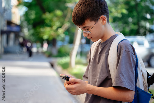 Photos School student in glasses with backpack using mobile map app on a city sidewalk while walking home after school, showing child independence, digital navigation, urban commute and safe travel
