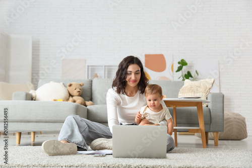 Cute little baby and happy young mother working with laptop on maternity leav...